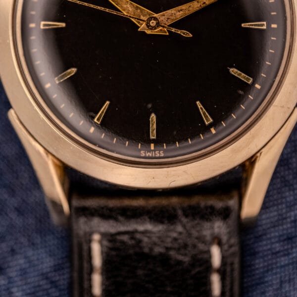 Close-up of a Tissot Automatic Bumper Cal. 28.5T wristwatch featuring a black dial, gold markers, black leather strap, and gold filled case with "SWISS" displayed.