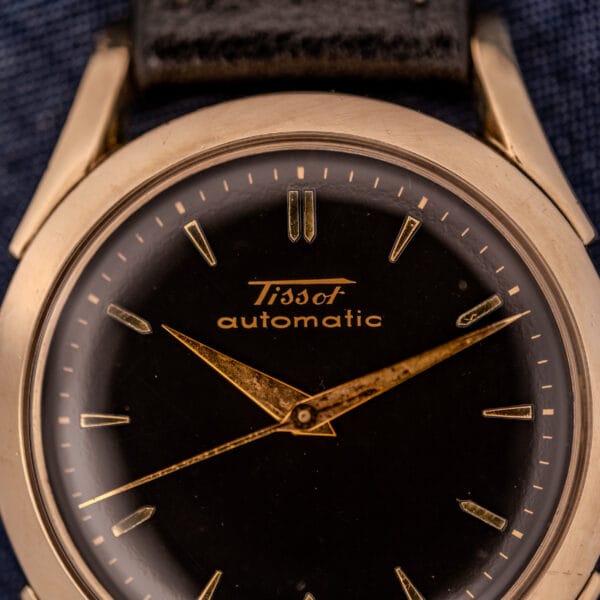Close-up of a Tissot Automatic Bumper wristwatch (Cal. 28.5T) with a black dial, gold filled case, and refined gold hands and markers.
