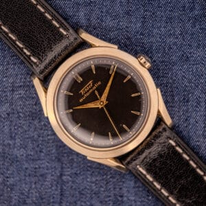 A vintage Tissot Automatic Bumper wristwatch, featuring a black dial and gold filled case (Cal. 28.5T), is displayed elegantly atop blue denim fabric.