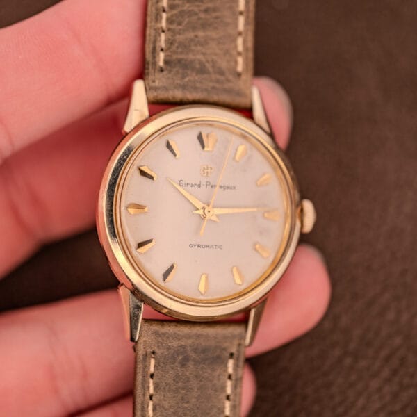 A hand holding a vintage Girard Perregaux Gyromatic Ref. B-1852 gold wristwatch with Automatic Cal. 21 movement and a brown leather strap.