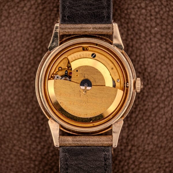 Close-up of a Girard Perregaux Gyromatic Ref. B-1852 Automatic Cal. 21 watch movement with a black leather strap, shown from the back on a brown surface.