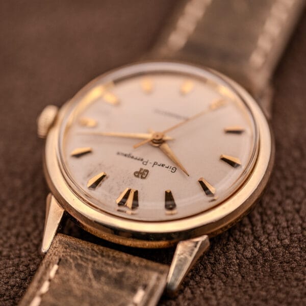 Close-up of a vintage Girard Perregaux Gyromatic Ref. B-1852 Automatic Cal. 21 wristwatch with a worn leather strap, shown resting on a brown surface.