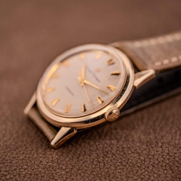 Close-up of a Girard Perregaux Gyromatic Ref. B-1852 Automatic Cal. 21 wristwatch with a gold case and brown leather strap, displayed on a textured brown surface.