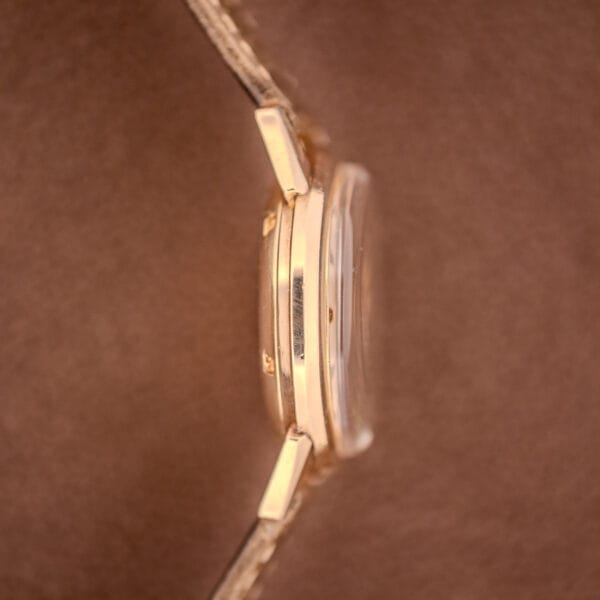 Side view of a Girard Perregaux Gyromatic Ref. B-1852 gold wristwatch with clear crystal and Automatic Cal. 21 movement, set against a soft brown background.