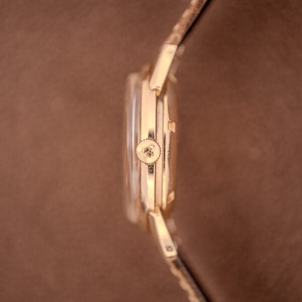 Side view of a Girard Perregaux Gyromatic Ref. B-1852 Automatic Cal. 21 wristwatch, featuring a gold case and textured crown, set against a brown background.
