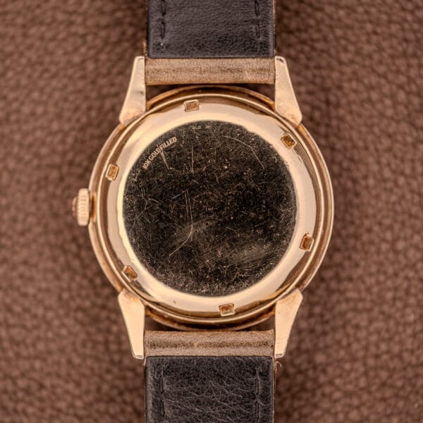 A close-up of the scratched gold back of a Girard Perregaux Gyromatic Ref. B-1852 Automatic Cal. 21 wristwatch with a black leather strap, shown on a brown surface.