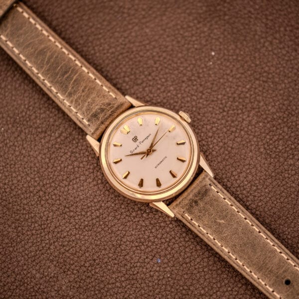 A vintage Girard Perregaux Gyromatic Ref. B-1852 with Automatic Cal. 21 movement and a brown leather strap, elegantly displayed on a textured brown surface.