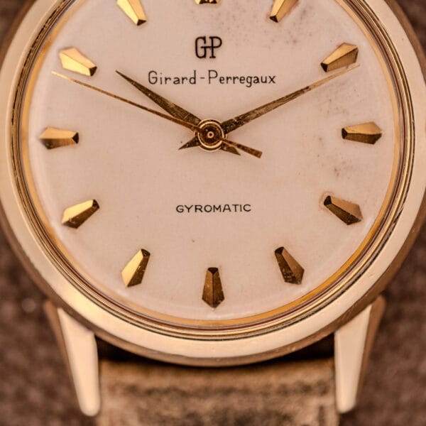 Close-up of a Girard Perregaux Gyromatic Ref. B-1852 wristwatch featuring gold hour markers and hands, powered by the Automatic Cal. 21 movement.