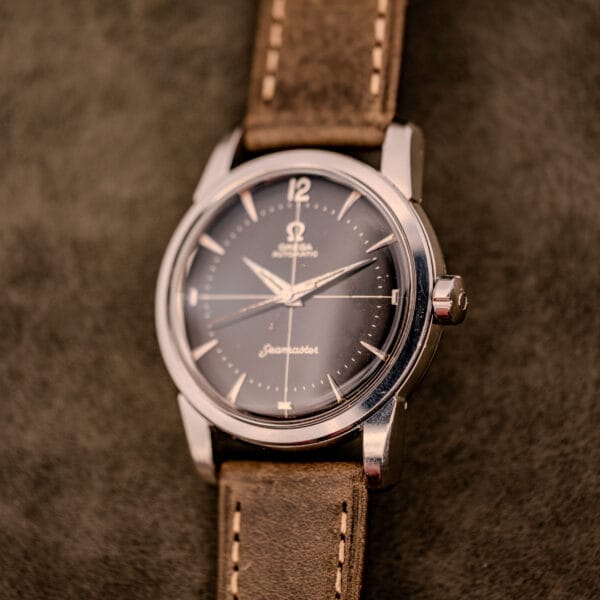 An Omega Automatic Seamaster Ref. 2848 Black Dial Cal. 500 wristwatch with a brown leather strap rests elegantly on a textured brown surface.