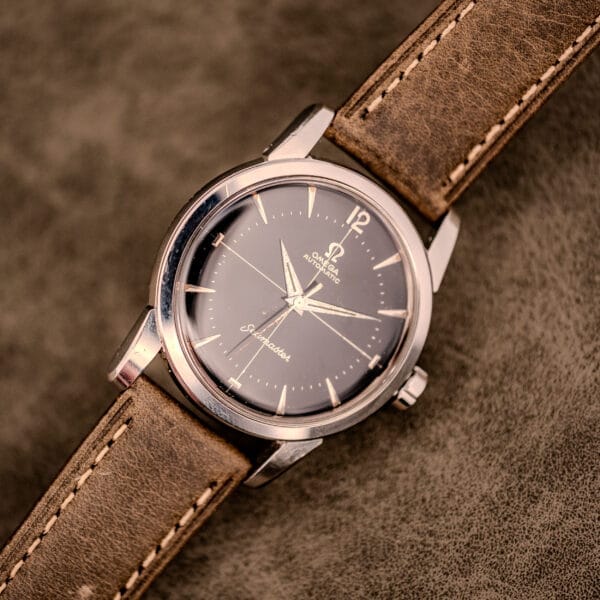 An Omega Automatic Seamaster Ref. 2848 Black Dial Cal. 500 wristwatch with a brown leather strap rests elegantly on a suede surface.