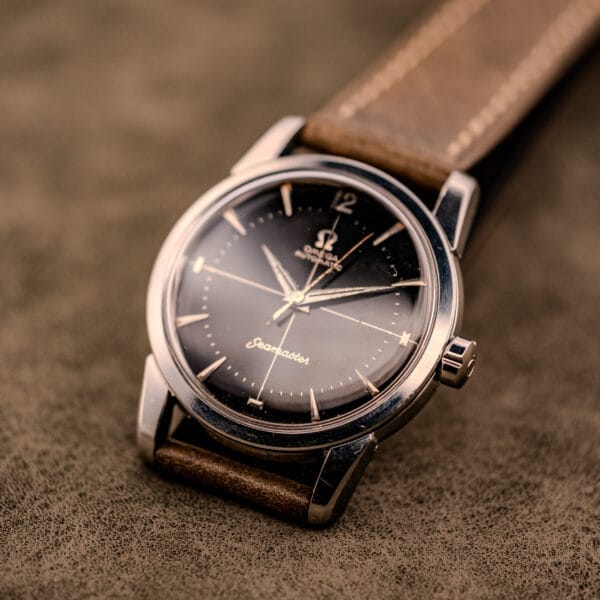 An Omega Automatic Seamaster Ref. 2848 Black Dial Cal. 500 wristwatch with a brown leather strap rests on a textured brown surface.