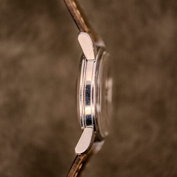 Side view of an Omega Automatic Seamaster Ref. 2848 Black Dial Cal. 500 wristwatch with a brown leather strap, set against a blurred brown background.