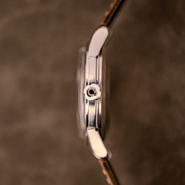 Side view of an Omega Automatic Seamaster Ref. 2848 Black Dial Cal. 500 wristwatch with a brown leather strap and silver case, set against a blurred brown background.