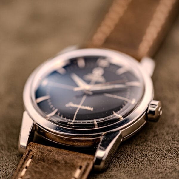A close-up of the Omega Automatic Seamaster Ref. 2848 with a black dial and brown leather strap, featuring Cal. 500, displayed on a textured surface.