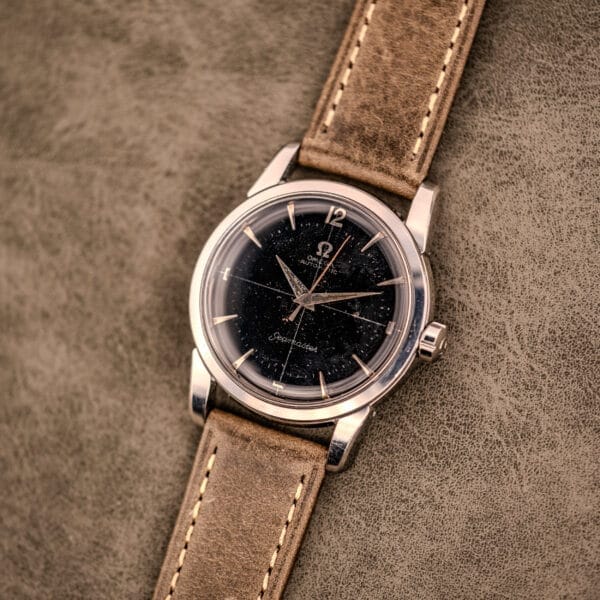 An Omega Automatic Seamaster Ref. 2848 Black Dial Cal. 500 wristwatch with a brown leather strap rests elegantly on a textured surface.