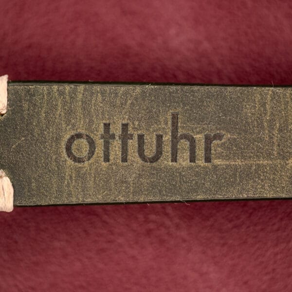 A wooden surface engraved with "ottuhr" against a red background, inspired by the elegance of the Longines Automatic Conquest Ref. 9000-1 14k Gold Capped Case.