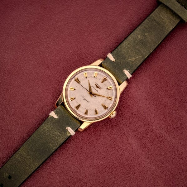 Longines Automatic Conquest Ref. 9000-1 wristwatch with a 14k gold capped case and green leather strap, displayed on a textured burgundy surface.