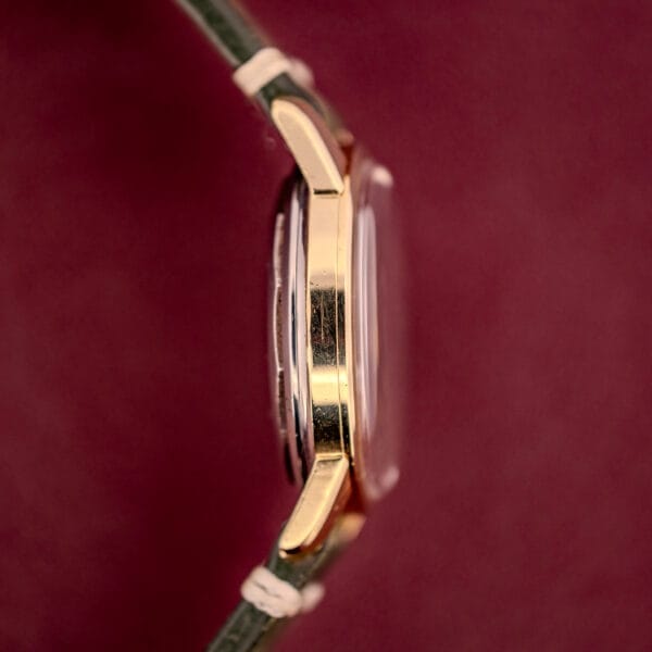 Side view of the Longines Automatic Conquest Ref. 9000-1 with a 14k gold capped case and leather strap, set against a burgundy background.