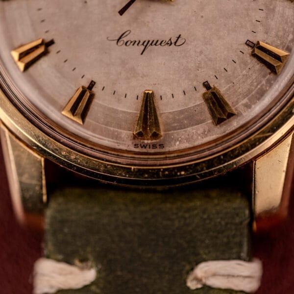 Close-up of the Longines Automatic Conquest Ref. 9000-1 with a 14k gold capped case, featuring Conquest and Swiss text on the dial, paired with a green leather strap.
