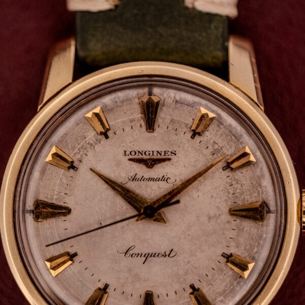 Close-up of a Longines Automatic Conquest Ref. 9000-1 wristwatch featuring gold markers, a worn white dial, and a classic 14k gold capped case.