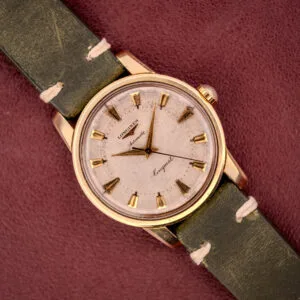 A Longines Automatic Conquest Ref. 9000-1 wristwatch with a 14k gold capped case and green leather strap, displayed on a maroon surface.