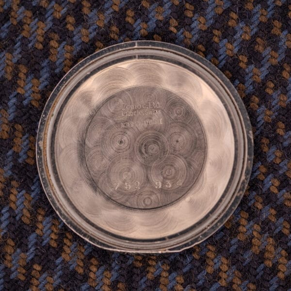 A round metal case back with engravings rests on textured blue and brown fabric—an original detail from the Zodiac Aerospace GMT Ref. 752-934 Black Dial & Chrome Bezel.