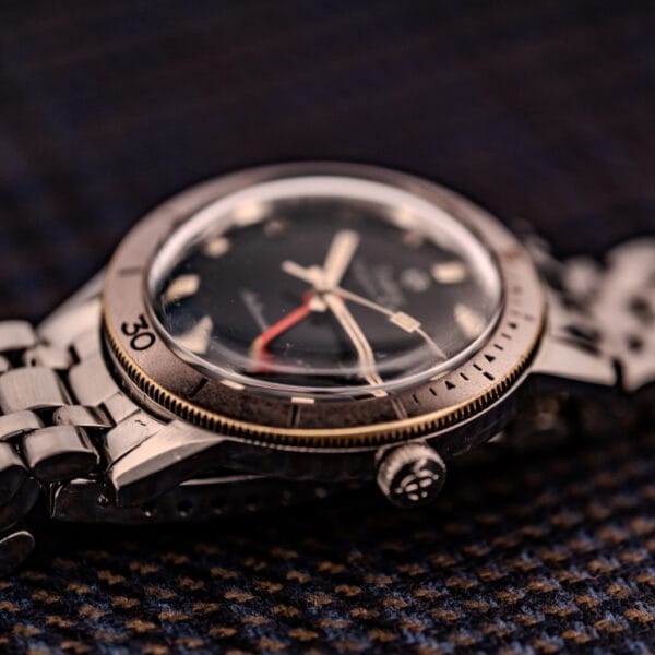 Close-up of a Zodiac Aerospace GMT Ref. 752-934 wristwatch with black dial and chrome bezel, featuring a metal band and resting on textured dark fabric.