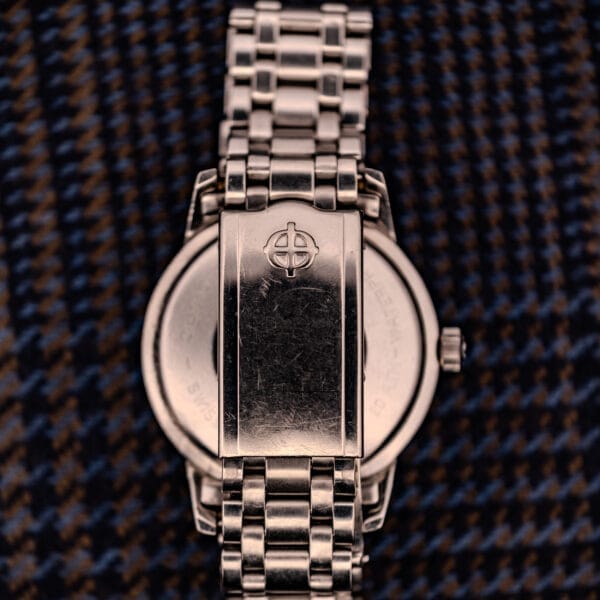 A Zodiac Aerospace GMT Ref. 752-934 with a black dial and chrome bezel, featuring a metal band, is shown from the back resting on patterned fabric.