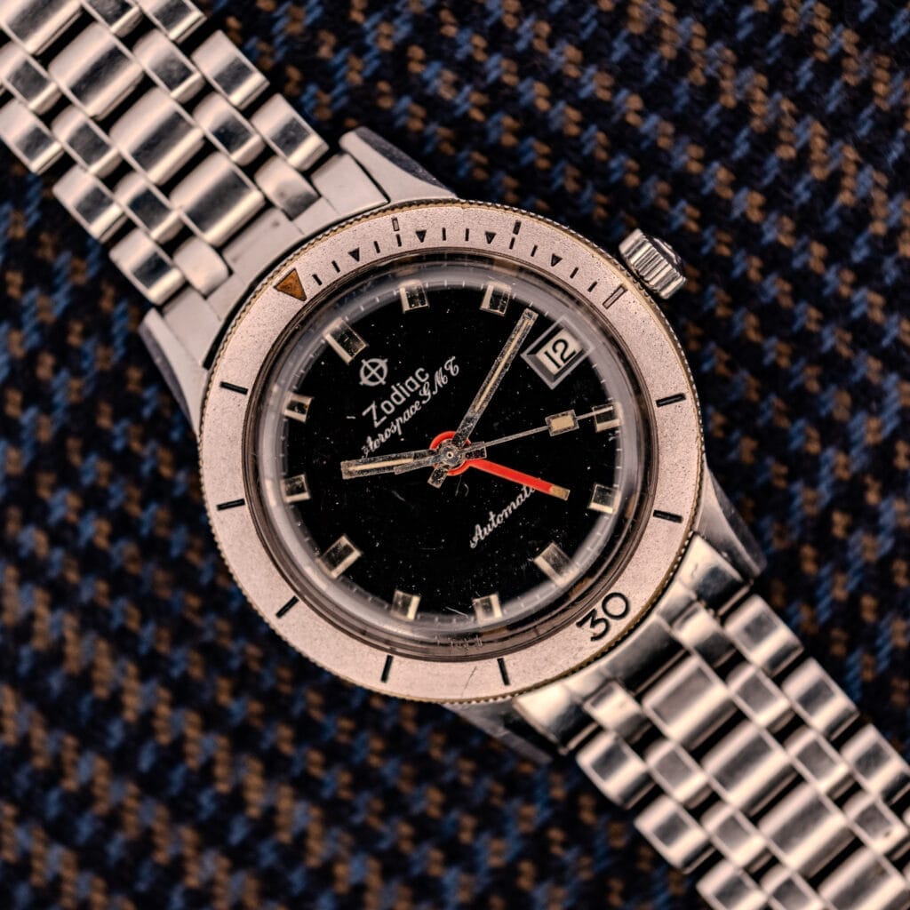 Zodiac Aerospace GMT Ref. 752-934 wristwatch with a black dial and chrome bezel, shown resting on patterned fabric.