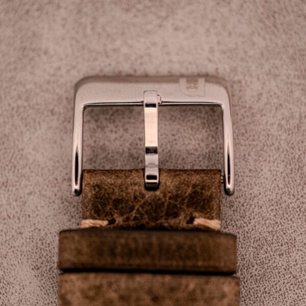 Close-up of a silver buckle on a brown leather strap, evoking the classic style of the Omega Seamaster Chronograph Ref. 145.016 Reverse Panda Dial.