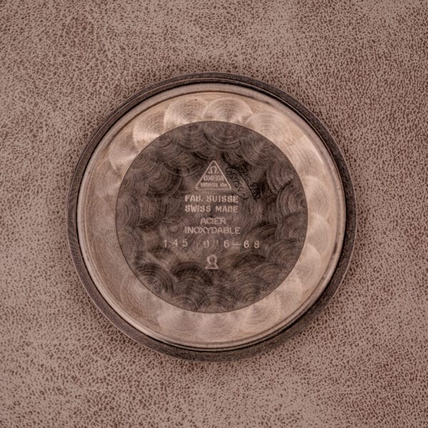 The Omega Seamaster Chronograph Ref. 145.016 Reverse Panda Dial watch case back is round with engraved markings, resting on a brown textured surface.