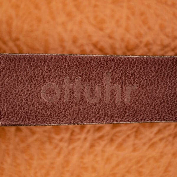 Close-up of a brown leather strap embossed with ottuhr, set against a textured orange background—perfectly complementing the Omega Automatic Seamaster Ref. 2849 Stainless Steel Chunky Lugs.