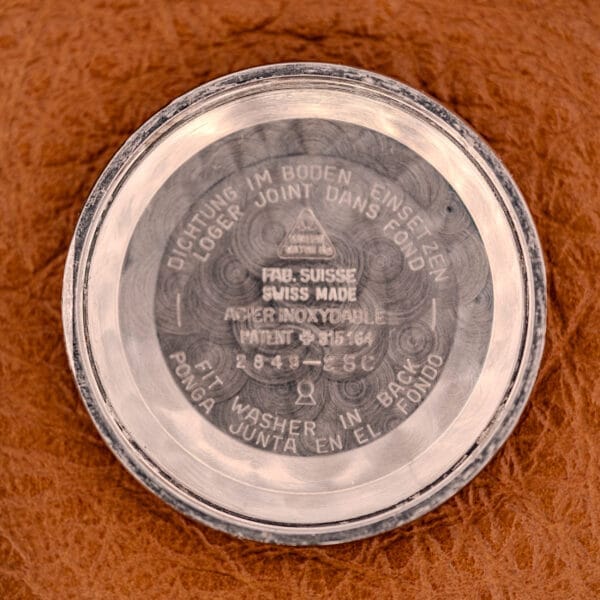 Close-up of an Omega Automatic Seamaster Ref. 2849 Stainless Steel Chunky Lugs case back with engraved text, displayed on a brown textured surface.