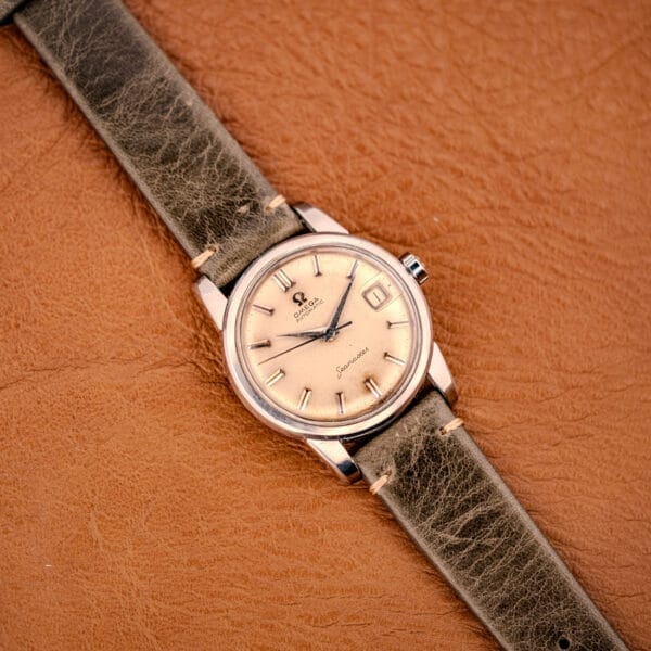 An Omega Automatic Seamaster Ref. 2849 Stainless Steel Chunky Lugs with a beige dial and leather strap, showcased on a textured brown surface.