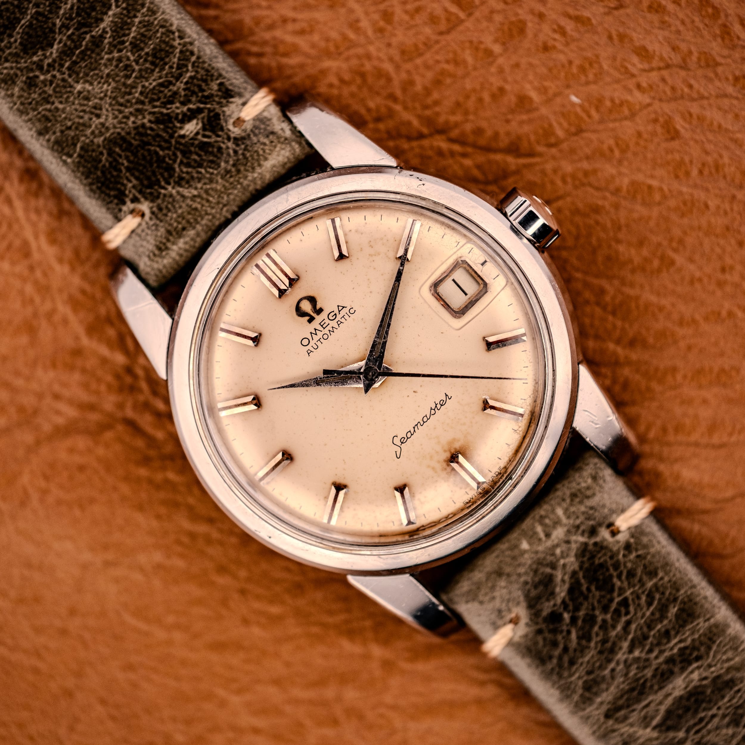 An Omega Automatic Seamaster Ref. 2849 Stainless Steel with chunky lugs is elegantly displayed on a brown surface, featuring a beige dial and leather strap. An Omega Automatic Seamaster Ref. 2849 Stainless Steel with chunky lugs is elegantly displayed on a brown surface, featuring a beige dial and leather strap.