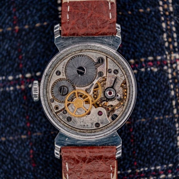 Close-up of the Movado "Acvatic" FB Case Sector Dial Ref. 11730 Cal. 150MN, showing its exposed mechanical gears and brown leather strap resting on plaid fabric.