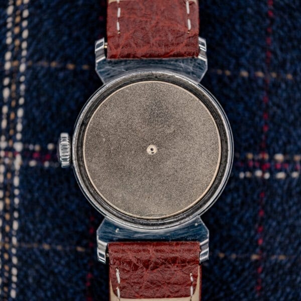 The Movado "Acvatic" FB Case Sector Dial Ref. 11730 Cal. 150MN features a blank face and brown leather strap, displayed on blue plaid fabric.