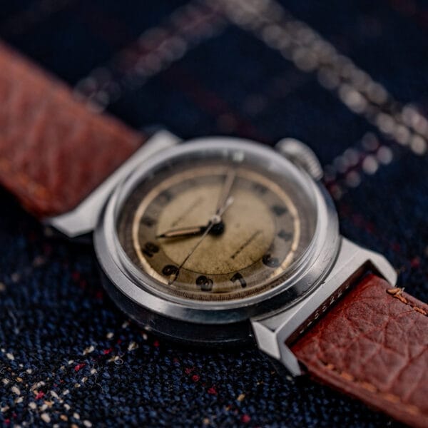 A Movado "Acvatic" FB Case Sector Dial Ref. 11730 Cal. 150MN wristwatch with a brown leather strap rests on dark plaid fabric, highlighting its vintage style.