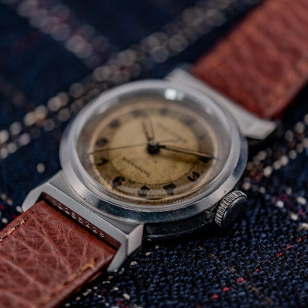 The Movado "Acvatic" FB Case Sector Dial Ref. 11730 Cal. 150MN, featuring a brown leather strap and vintage sector dial, rests on a dark textured fabric.