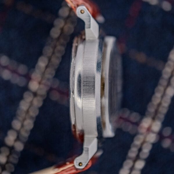 Side view of a Movado "Acvatic" FB Case Sector Dial Ref. 11730 Cal. 150MN wristwatch with metal case and brown leather strap on a dark plaid fabric background.