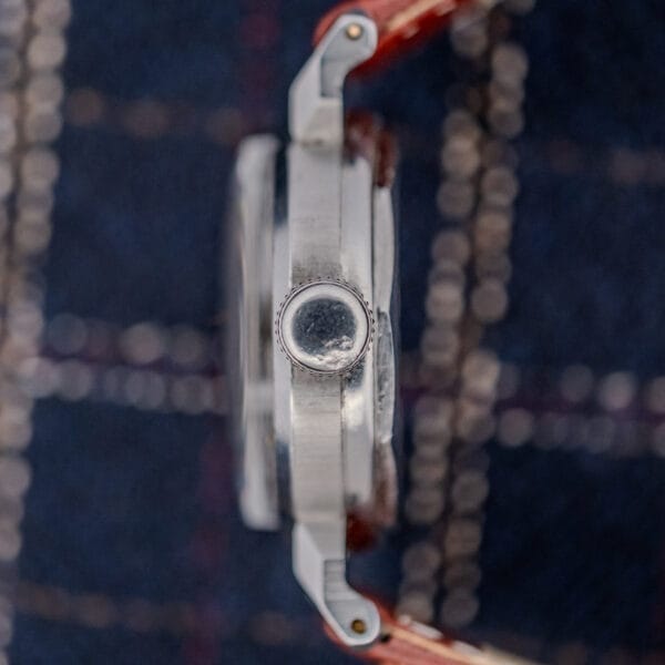 Side view of a silver Movado "Acvatic" FB Case Sector Dial Ref. 11730 Cal. 150MN wristwatch with a brown strap, displayed on dark plaid fabric.