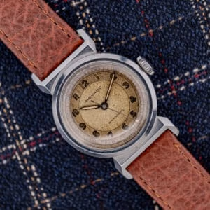 A Movado "Acvatic" FB Case Sector Dial Ref. 11730 Cal. 150MN wristwatch with a brown leather strap rests on a blue plaid fabric background.