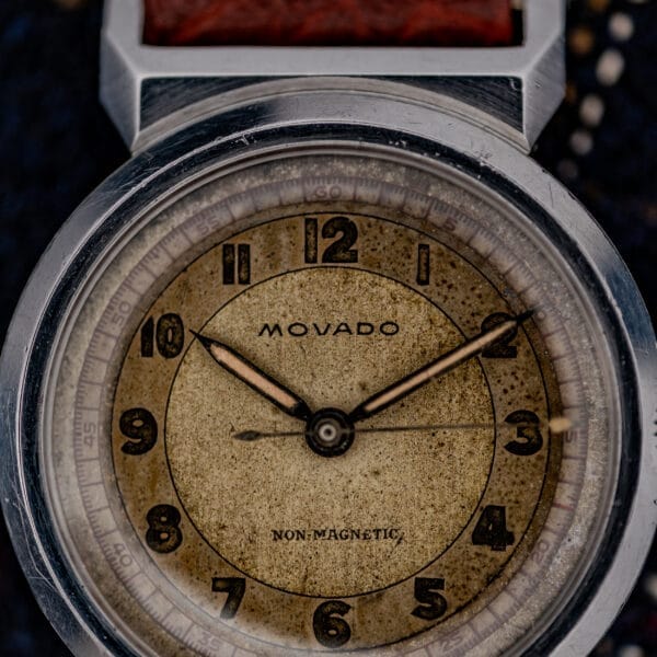 Close-up of a vintage Movado "Acvatic" Ref. 11730 FB case wristwatch with a worn beige Sector Dial, black numerals, and Cal. 150MN, displaying the time at 10:09.