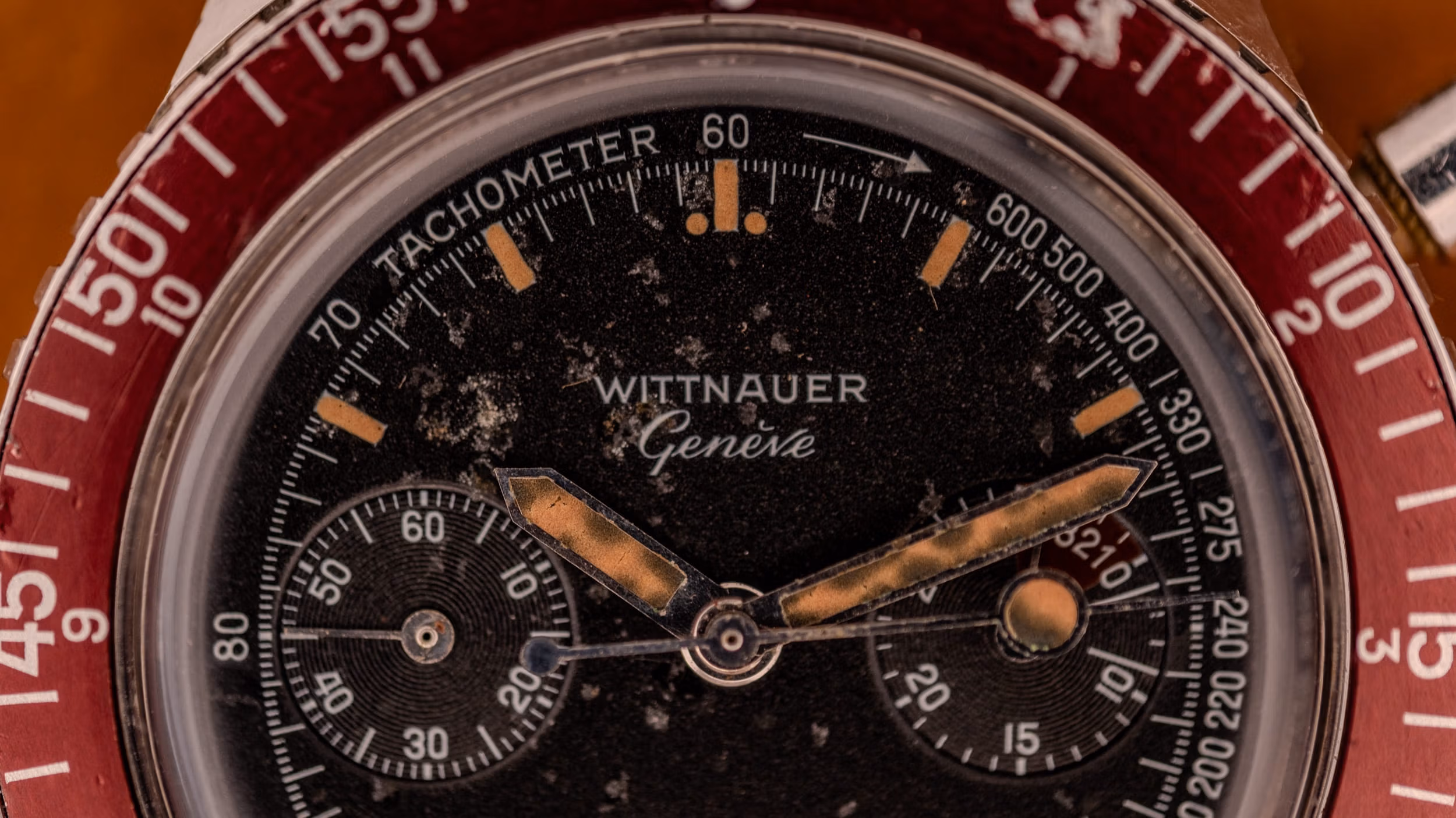 Close-up of a vintage Wittnauer watch face with worn black dial and red tachymeter bezel, serving as a guide to classic timepiece design.