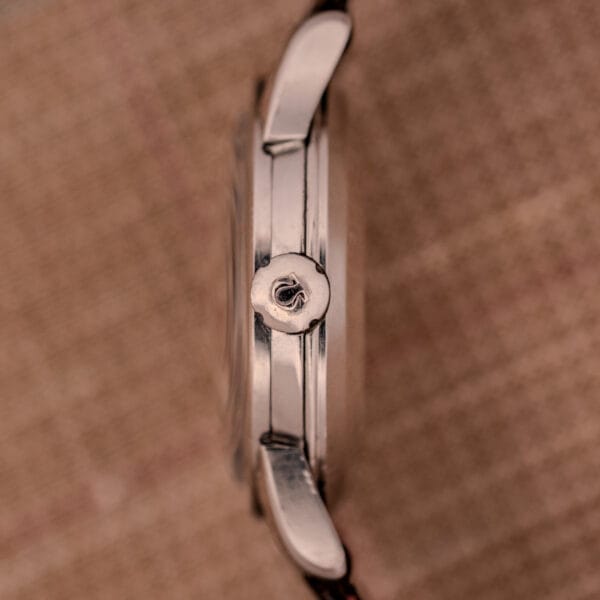 Side view of a 1956 Omega Seamaster Automatic Ref. 2828-6 SC Cal. 470 in stainless steel, showing its silver case and textured crown, set against a brown fabric background.