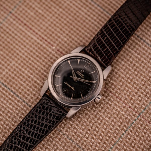 1956 Omega Seamaster Automatic Ref. 2828-6 SC Cal. 470 Stainless Steel watch with a black dial and brown textured leather strap, displayed on a plaid fabric background.