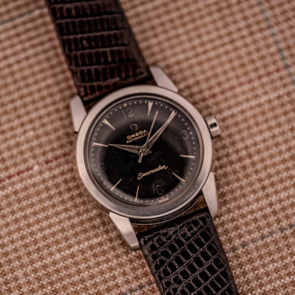 1956 Omega Seamaster Automatic Ref. 2828-6 SC Cal. 470 stainless steel wristwatch with a black dial and brown textured leather strap, displayed on plaid fabric.