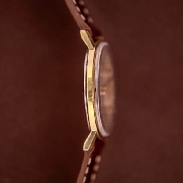 Close-up side view of a Hamilton Manual Wind Cal. 638 Sunburst Dial gold tone case wristwatch with a brown leather strap and white stitching.
