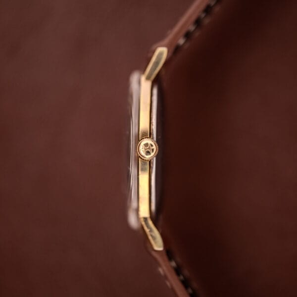 Side view of a Hamilton Manual Wind Cal. 638 Sunburst Dial wristwatch, featuring a gold tone case and brown leather band, set against a brown background.