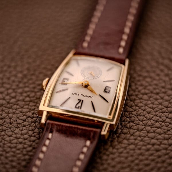 Hamilton Asymmetric Khyber Manual Wind Caliber 730 wristwatch with a brown leather strap, shown on a textured brown surface.